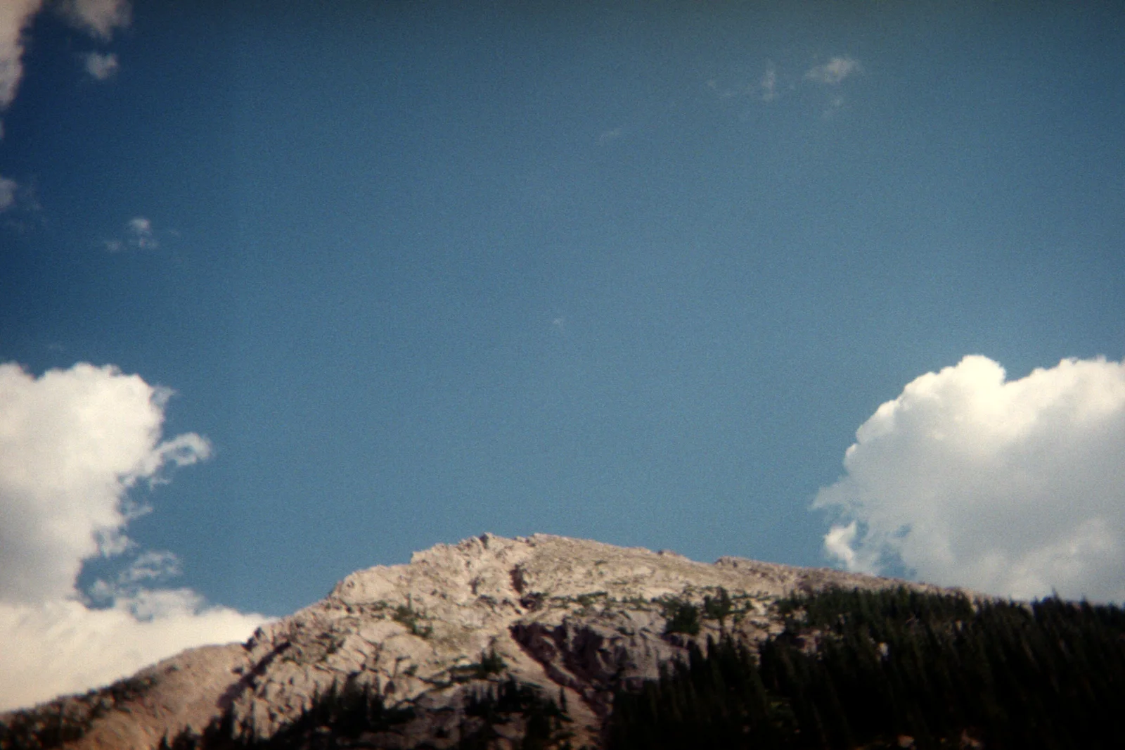 A rocky summit under deep blue sky with two white clouds, shot on film.