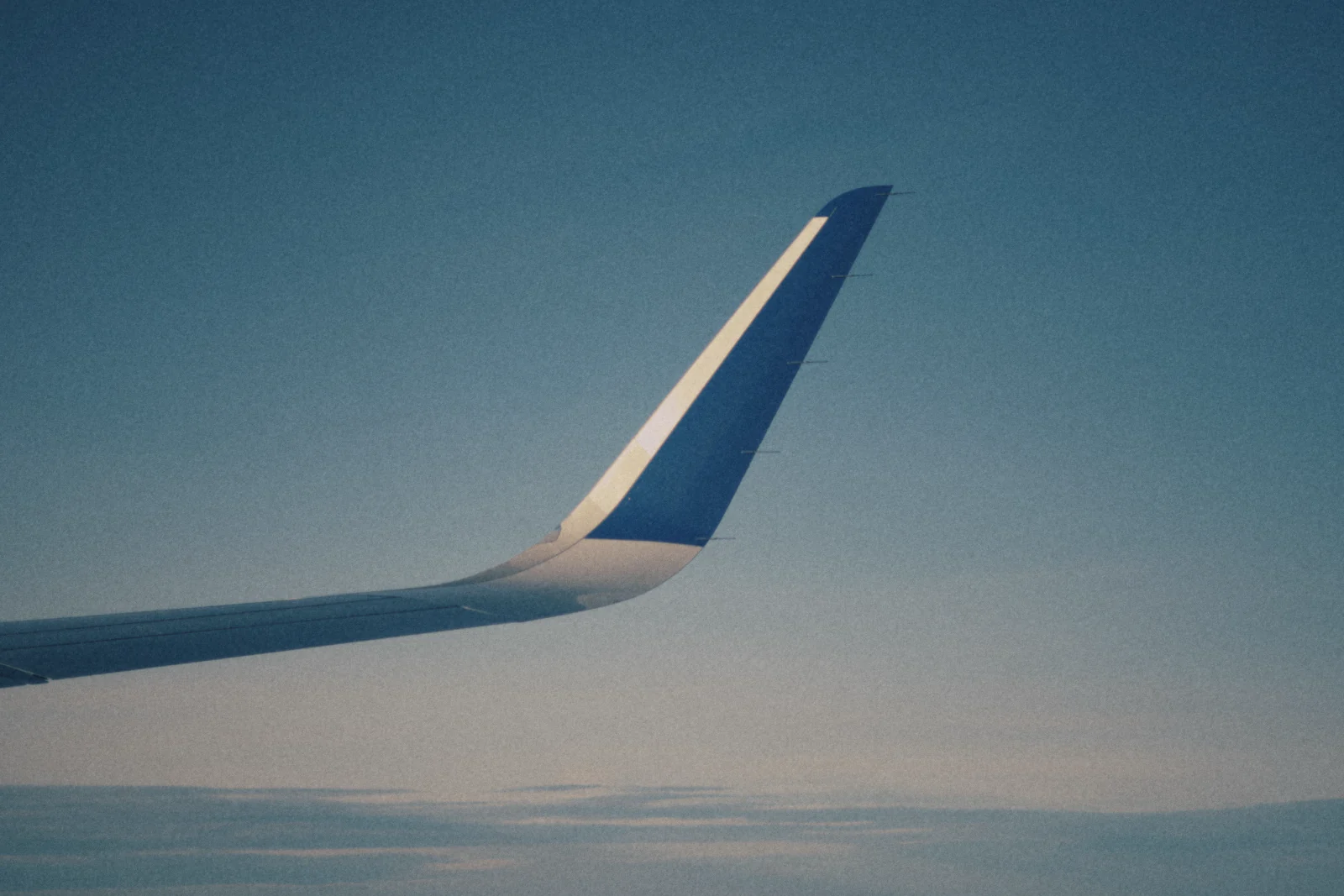 An airplane wingtip above a soft, hazy horizon.